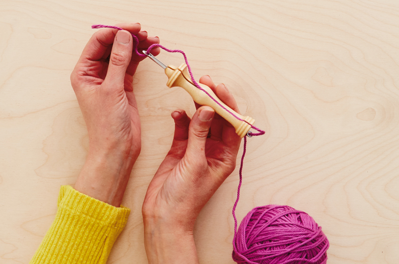A woman's hands thread a punch needle with magenta colored yarn.
