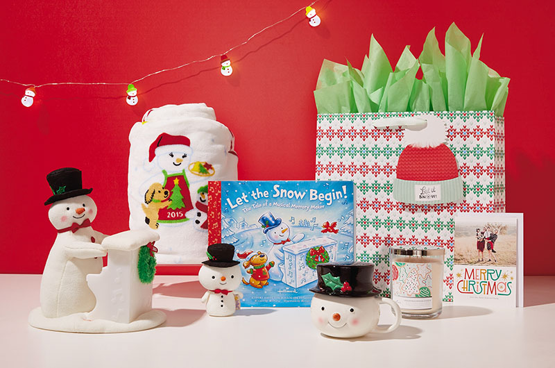 A snowman-themed care package featuring an interactive plush snowman with a matching book, a snowman mug, a Christmas cookie 3-wick candle, a personalized photo card, a cozy fleece snowman blanket, a snowman itty bittys, and a gift bag covered in an argyle sweater pattern with a gift tag that looks like a pompom knit stocking cap.