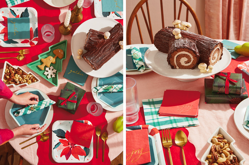 A Christmas tablescape featuring Hallmark Celebrate! partyware products like dark green hexagon-shaped plates and dark green and white plaid napkins; at the center of the table is a traditional yule log cake covered in chocolate frosting and meringue marshmallows, sitting on a simple white cake stand; nearby is a set of mod gold candle holders with white, twisted candles in them.