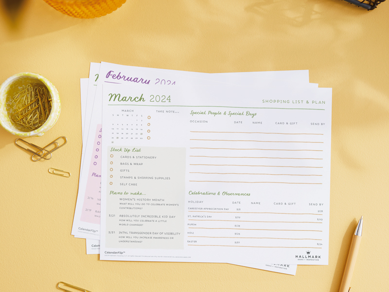 A printed March 2024 celebration planner page sitting on a home office desktop, surrounded by desk accessories.