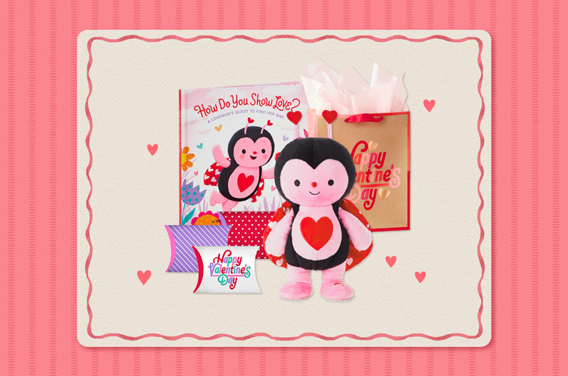 A collection of Valentine's Day gifts for a child that includes a plush, interactive ladybug that dances and sings, along with a coordinating book, a set of pillow boxes in red, purple, pink and white that are filled with treats, and a brown kraft paper gift bag with red edging that reads, 