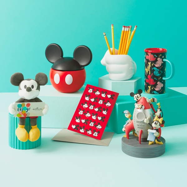 A selection of gifts meant for a parent who loves Disney, including a small plush Disney Mickey Mouse gift card holder, a sculpted pencil holder in the shape of Mickey's gloved hand, a color-changing travel mug featuring the faces of Mickey Mouse, Minnie Mouse, Donald Duck and Goofy; a treat jar with a lid that looks like black Mickey Mouse ears; a figurine of Mickey, Minnie, Donald and Goofy prepping a vintage-looking spaceship for launch; and a greeting card featuring the face of Mickey Mouse in a variety of different expressions on top of a red background.