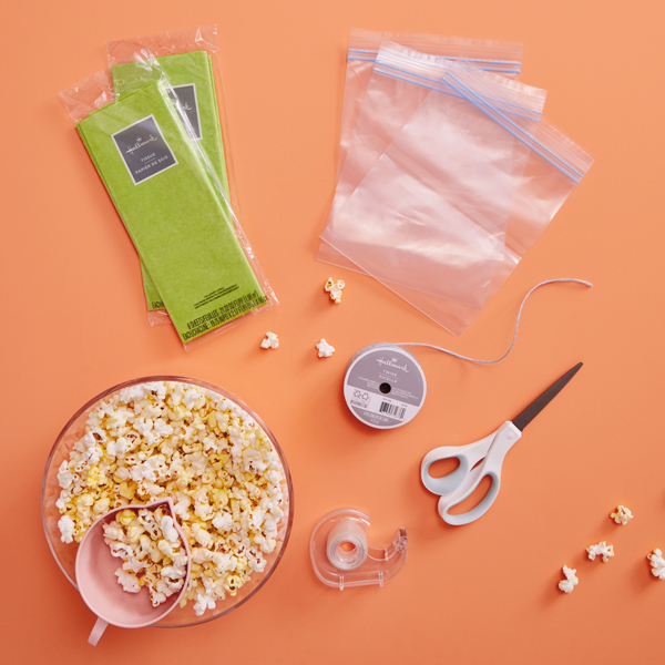 Supplies needed for the cornhusk popcorn party favor include green tissue paper, plastic zipper sandwich bags, tape, scissors, twine, and popcorn.