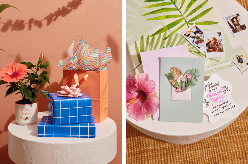 Two gifts wrapped in cobalt blue wrapping paper with a white grid print sit on a white sidetable; next to the stacked gifts are a white planter with a message on the side that reads, 