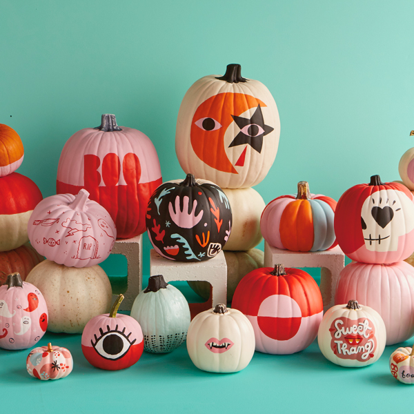 A large assortment of painted pumpkins is displayed against a teal background.