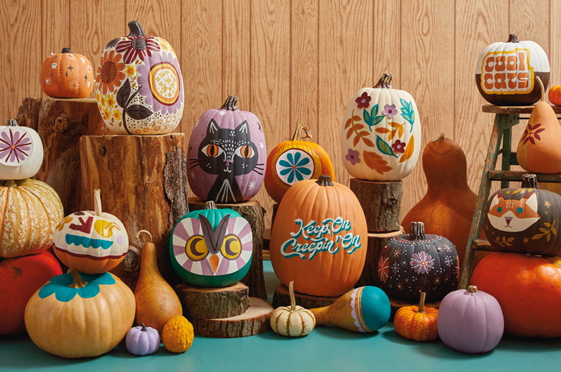 A large assortment of painted pumpkins is displayed against a wood background.