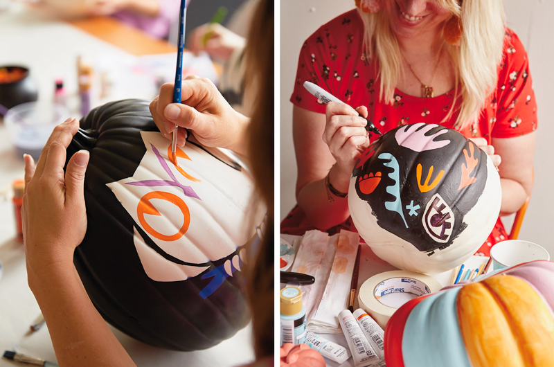 A woman paints on a black pumpkin.