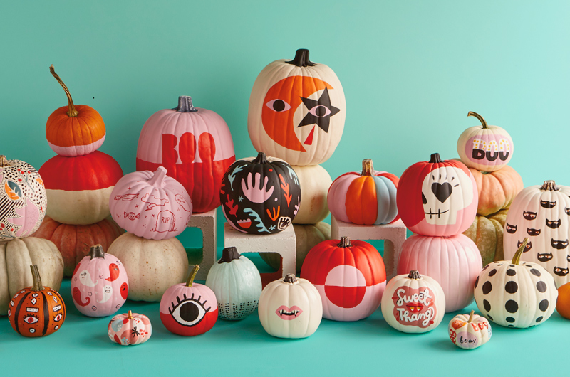 A large assortment of painted pumpkins is displayed against a teal background.