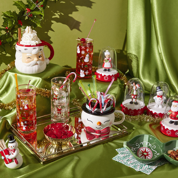 A table decorated with Christmas-themed glassware, mugs and serving dishes, with a shiny, green, satin tablecloth.