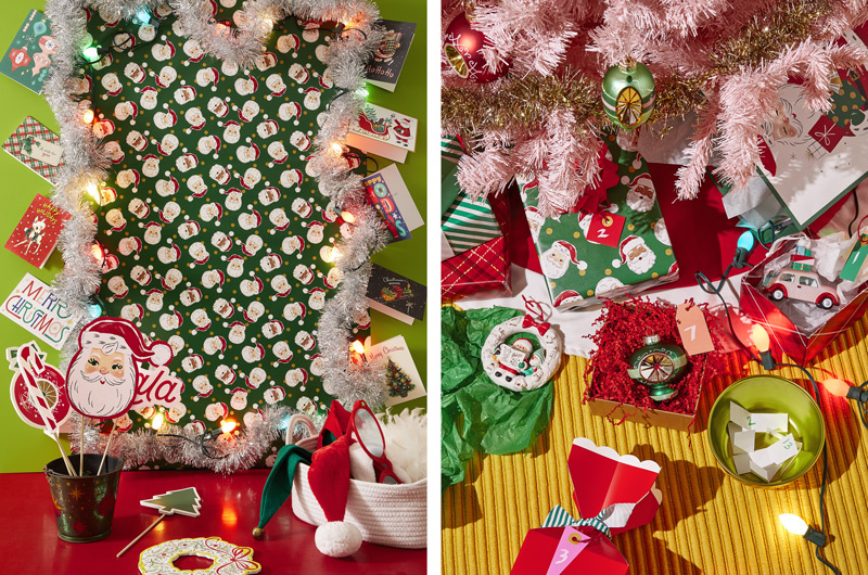 A holiday selfie station with a background made of holiday gift wrap and silver tinsel garland; a basket of props like silly glasses, a Santa hat and an elf hat lay nearby; around the selfie background, several holiday cards are taped to the wall; next to this scene is a gift exchange setup with a pastel pink Christmas tree and numbered boxes holding Christmas ornaments.