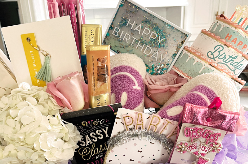 A gift basket full of birthday cards, chocolate bars and small gifts like flowers, cozy slippers and a keychain.