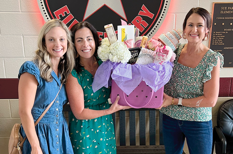 Social media influencer Leanna Laming stands with two of her friends, holding a large gift basket full of cards, chocolate bars and small gifts between them.