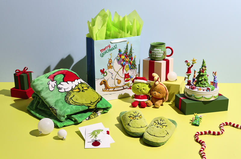 A Christmas care package with a Dr. Seuss The Grinch theme that includes a fleece throw blanket, fuzzy Grinch slippers, a Keepsake Ornament, a Grinch and Max Better Together magnetic plush pair, a table figurine, a mug, and a gift bag and greeting card that feature the Grinch.