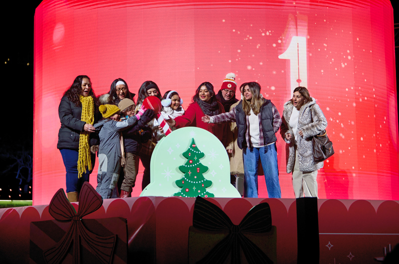 Two families stand on stage at the Hallmark Christmas Experience, preparing to pull an enormous lever that lights a towering Christmas tree in Crown Center Square.