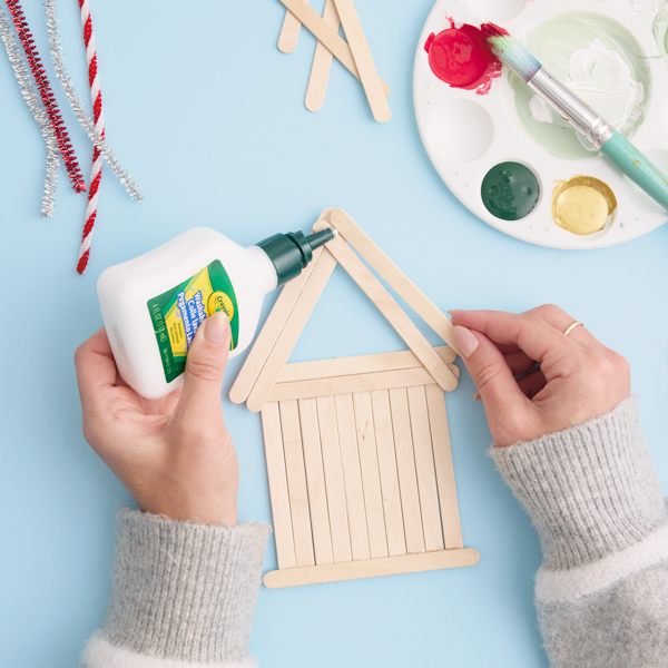 A woman's hands glue wooden popsicle sticks into a house shape.