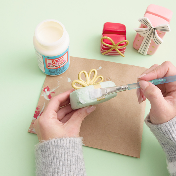 A woman paints her finished Christmas card display stand made of air-dry modeling clay with a layer of glossy Mod Podge.