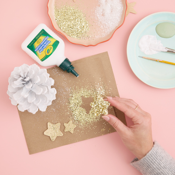 A woman's hands apply craft glue and gold glitter to a star-shaped piece of paperboard..