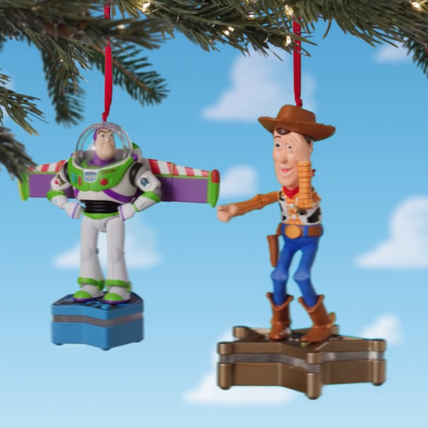 Two Keepsake Ornaments, one featuring the character Woody and the other featuring the character Buzz Lightyear from the Disney Pixar movie Toy Story, hang from a Christmas tree branch.