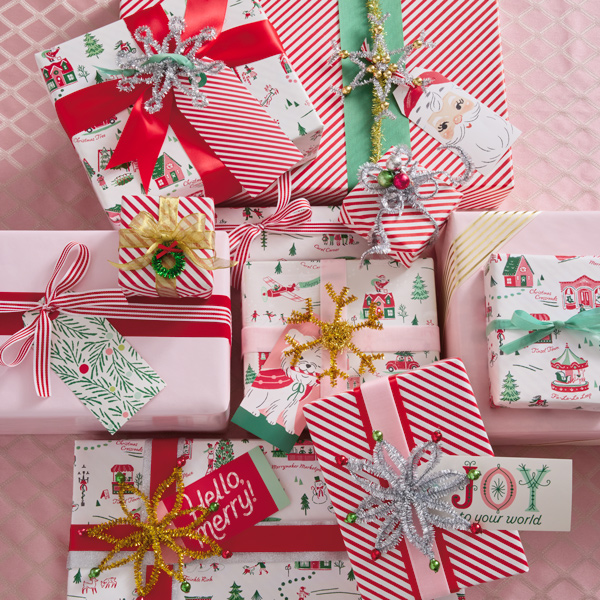 A collection of Christmas gifts wrapped in vintage-style wrap in shades of red, white and pink, with metallic pipe cleaner embellishments shaped like stars, snowflakes and wreaths.