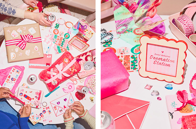A downshot of a small white table top surrounded by a group of girlfriends who are decorating their Secret Valentine gifts before their exchange.