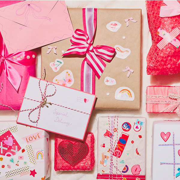 A collection of gifts at a Secret Valentine party, decorated with different kinds of wrap in shades of pink, red, white and kraft paper brown, wrapped with ribbons of different widths and materials in pink, red and white patterns, and covered in fun Valentine's Day-themed stickers.