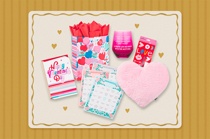 A selection of Valentine's Day gift ideas for a friend, including a pink, plush, heart-shaped pillow; a deep pink stemless wine glass that reads, 
