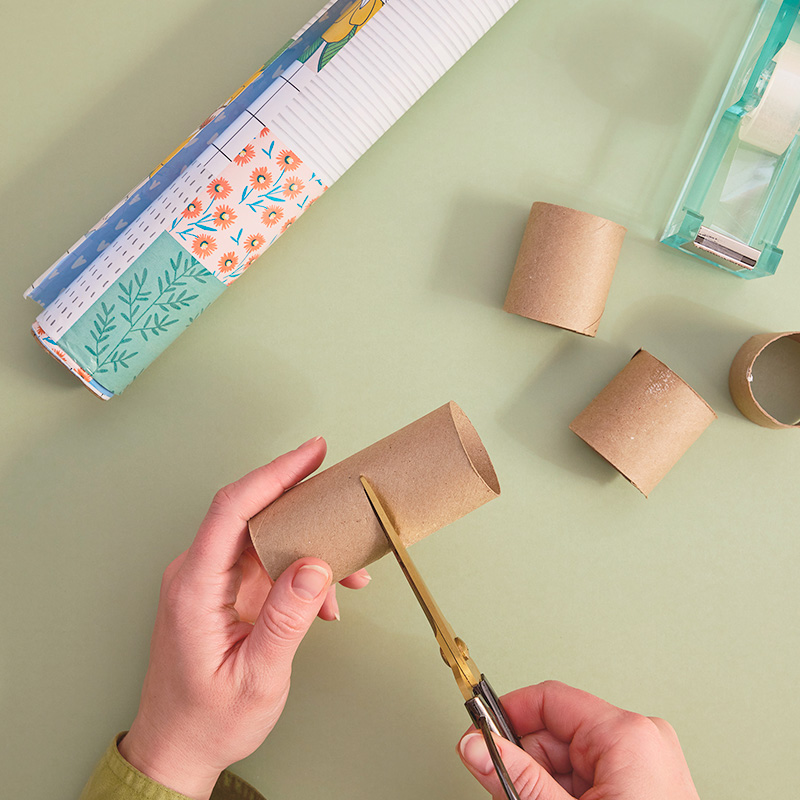 A woman's hands are shown using scissors to cut cardboard tubing into two-inch sections.