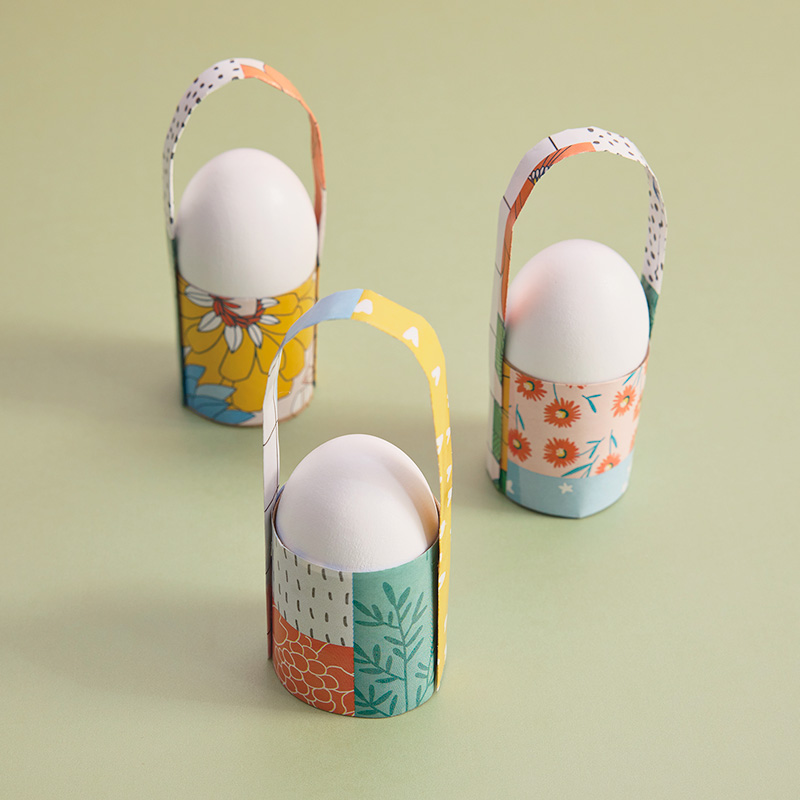 Three individual egg holders that look like little baskets sit on a light pistachio green surface.