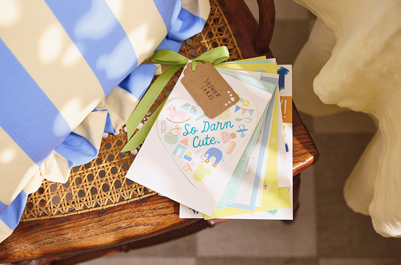 A bundle of greeting cards received at the baby shower have been hole-punched in the top left corner and strung together with ribbon, along with a tag that reads, 