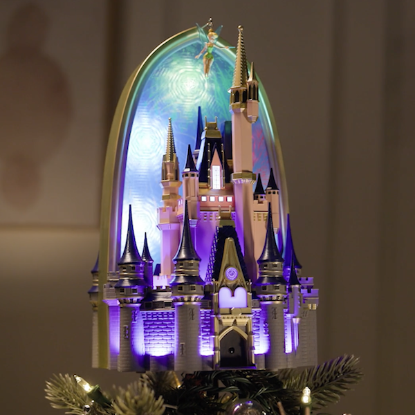 A Keepsake tree topper in the form of the iconic Cinderella Castle from Walt Disney World Magic Kingdom; the tree topper is light from both within the castle and in the archway of artificial sky above; Tinkerbell hovers over the scene.