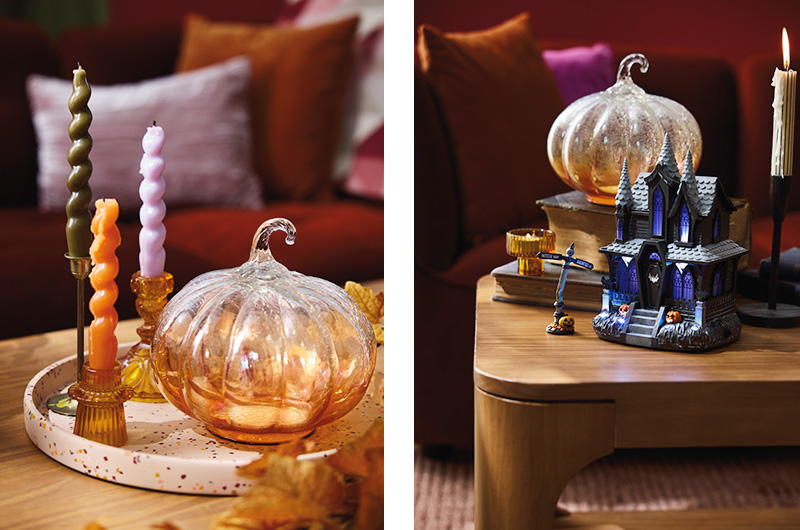 Two small home decor setups are positioned side by side; on the left is a fall decor setup featuring a glass pumpkin on a white tray flecked with fall colors, with a trio of candles in candlesticks sitting nearby; on the right is a demonstration of how that glass pumpkin can also work for Halloween decor, with the tray and candlesticks removed and a light-up haunted house figurine swapped in.