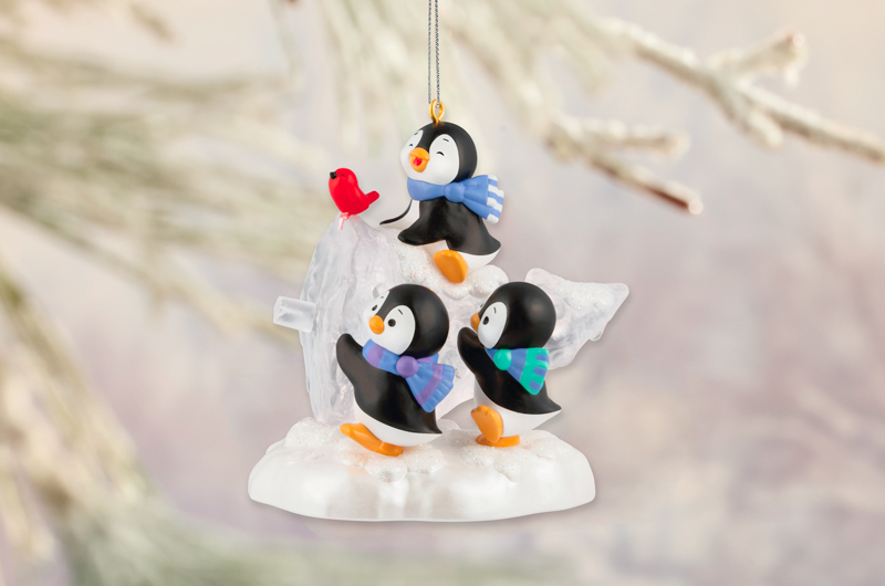 A Keepsake Ornament featuring a trio of adorable little penguins wearing scarves; the penguins are carrying home a Christmas tree that they've chopped down.