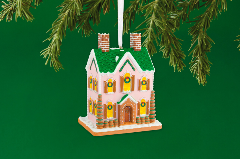 A Keepsake Ornament in the form of an ornate gingerbread house covered with light pink icing, green candy-tiled roof and detailed white piping accents.
