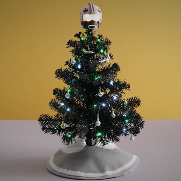 A miniature black Christmas tree decorated with an interactive Star Wars Rebel Alliance flight helmet tree topper, a mini Rebel Alliance tree skirt, and silver X-Wing Starfighter and Millennium Falcon ornaments.