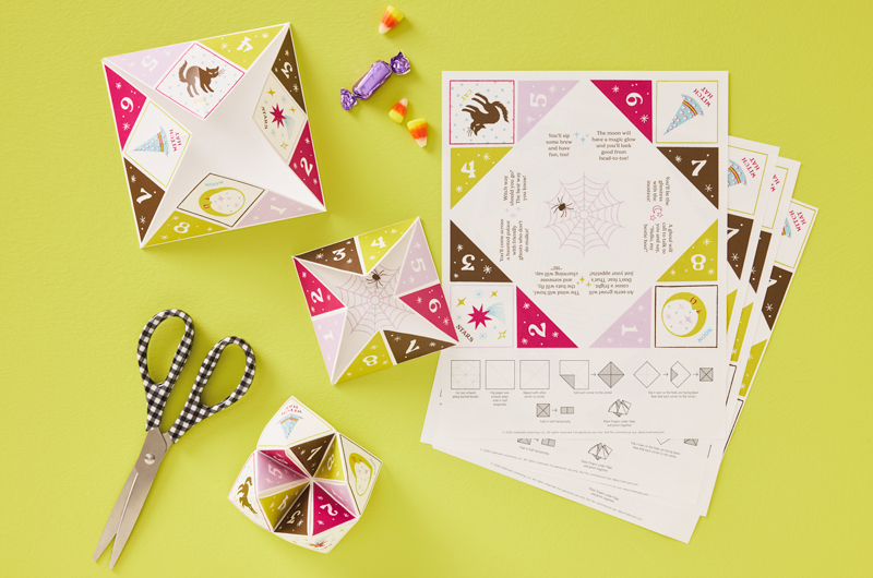 Copies of our free origami fortune teller activity printable lay splayed out on a lime-green surface; near the copies are three examples of the activity in different stages of being folded up, per the directions on the page.