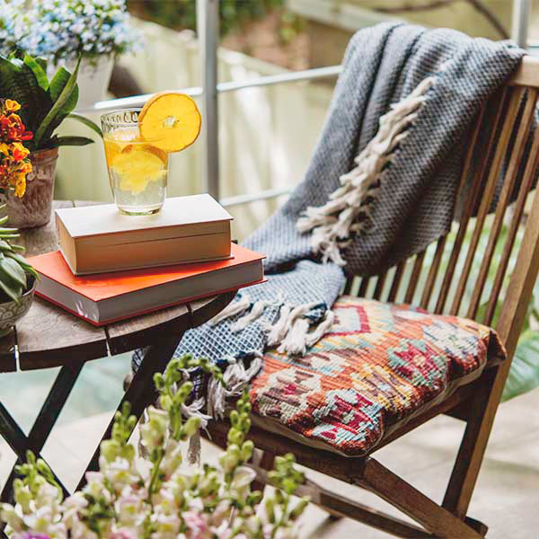 A cushioned patio chair sits next to a small wooden table; atop the table are two books and a glass of water with lemon slices.
