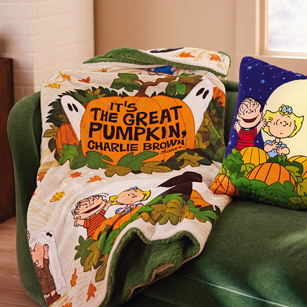 A fleece throw and a throw pillow lay on a green couch; the throw and pillow feature scenes from the classic Halloween television special, 
