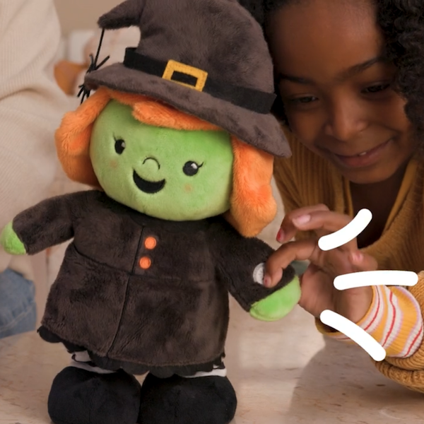 A little girl reaches to push a button on the hand of an interactive plush Halloween witch that sings and dances to the tune of 