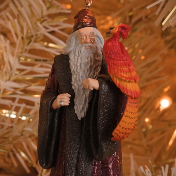 A Keepsake Ornament featuring the likeness of the character Albus Dumbledore from the movie Harry Potter and the Chamber of Secrets hangs from the branch of a Christmas tree.
