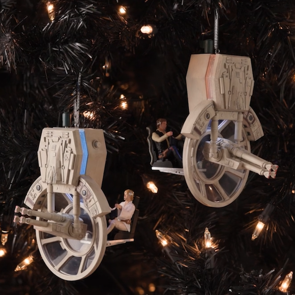Two Keepsake Ornaments featuring the characters Han Solo and Luke Skywalker hang from branches on a Christmas tree; the ornaments reenact a scene where the Rebels have escaped the Death Star and encounter a squad of TIE Fighters; Luke and Han sit in the seats of the Millennium Falcon's laser turrets.