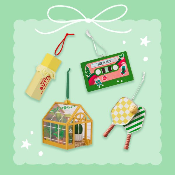 Assortment of Christmas ornaments including a butter stick, a holiday cassette tape, a miniature greenhouse, and a pickleball paddle set arranged on a mint-green background with decorative white doodles.