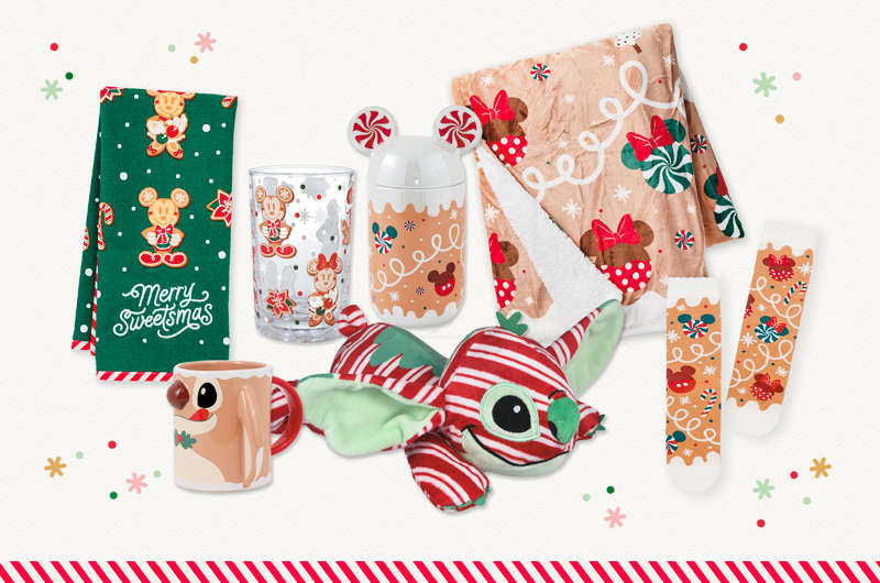 A collection of Disney-themed gift product with a Christmas gingerbread or sweets theme, with patterns that reference Disney characters like Mickey Mouse, Minnie Mouse and Stitch; products include a tea towel; a ceramic mug; a clear drinking glass with a pattern applied to it; a covered mug with a lid shaped like Mickey Mouse ears; a fleece blanket with a Christmas sweets pattern; and a pair of socks with a similar Christmas gingerbread and sweets pattern.