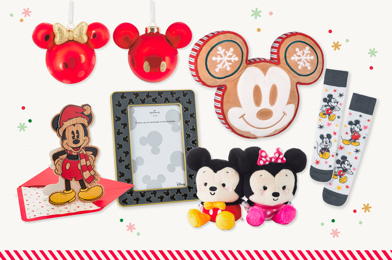 A collection of Disney-themed products, including: a pair of matching glass orb ornaments that look like Mickey Mouse and Minnie Mouse ears; a decorative pillow that looks like Mickey Mouse's head and face, with a Christmas gingerbread and sweets motif; a pair of socks with illustrations of Mickey Mouse on the cuffs; a pair of magnetic plushies in the shape of Mickey Mouse and Minnie Mouse; a picture frame with a gray border and a black Mickey Mouse ears silhouette print; and a Christmas card with a wooden front shaped like Mickey Mouse wearing a Santa hat, and can stand on display.