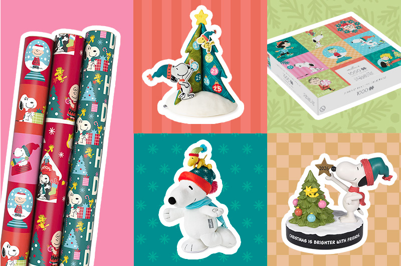 Peanuts holiday-themed gift collection featuring three rolls of wrapping paper with Snoopy and winter character illustrations, a Snoopy advent calendar shaped like a Christmas tree with numbered doors, a puzzle box displaying a four-panel holiday scene, and two Snoopy Christmas ornaments. One ornament shows Snoopy wearing earmuffs with a small bird on top, and the other features Snoopy beside a decorated tree with the visible text “2026” and “CHRISTMAS IS BRIGHTER WITH FRIENDS.”