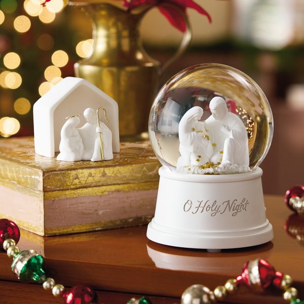 Two decor items made of white ceramic—one a water globe with gold stars floating in it, the other a simple, two-piece tabletop figurine set—depict the Nativity, with Joseph kneeling near Mary as she sits holding the baby Jesus.