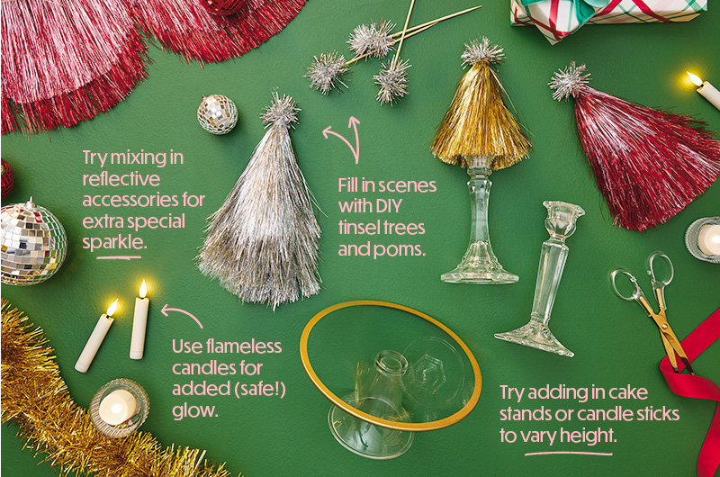 Holiday craft supply flat lay featuring tinsel trees, pom-pom picks, flameless candles, glass candleholders, ribbon, scissors, and reflective ornaments arranged on a green background. Printed tips throughout the image explain how to mix in reflective accessories for sparkle, fill scenes with DIY tinsel trees and poms, use flameless candles for added glow, and add cake stands or candlesticks to vary display height.